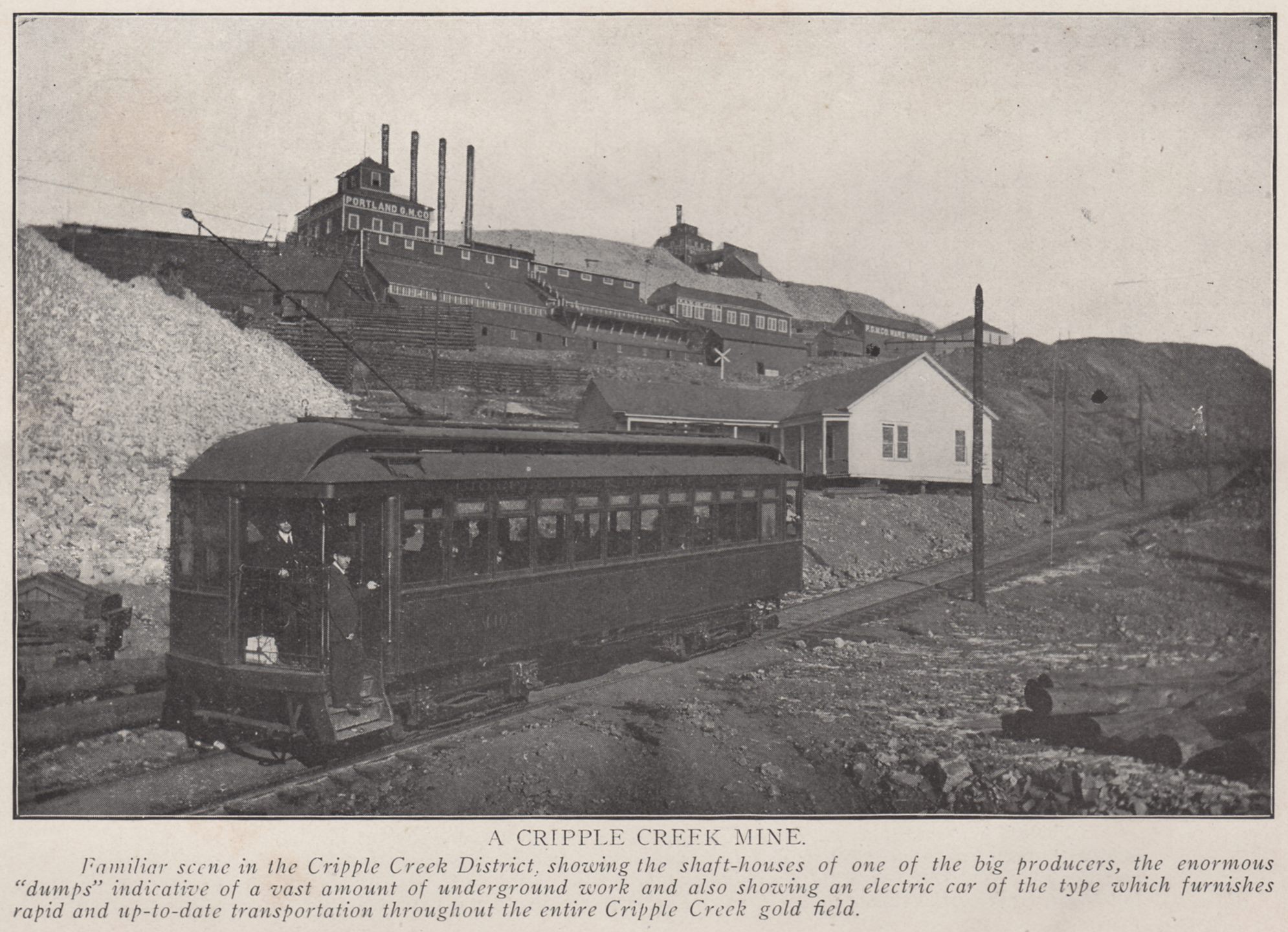    Familiar scene in the Cripple Creek District, showing the shaft-houses of one of the big producers, the enormous ''dumps'' indicative of a vast amound of underground work and also showing an electric car of the type which furnishes rapid and up-to-date transportation throughout the entire Cripple Creek gold field.
-> This is along the original High Line, just before it crosses over the M.T. mainline on its way down Battle Mountain. The mines in the background is the Portland Nos. 1 & 2.