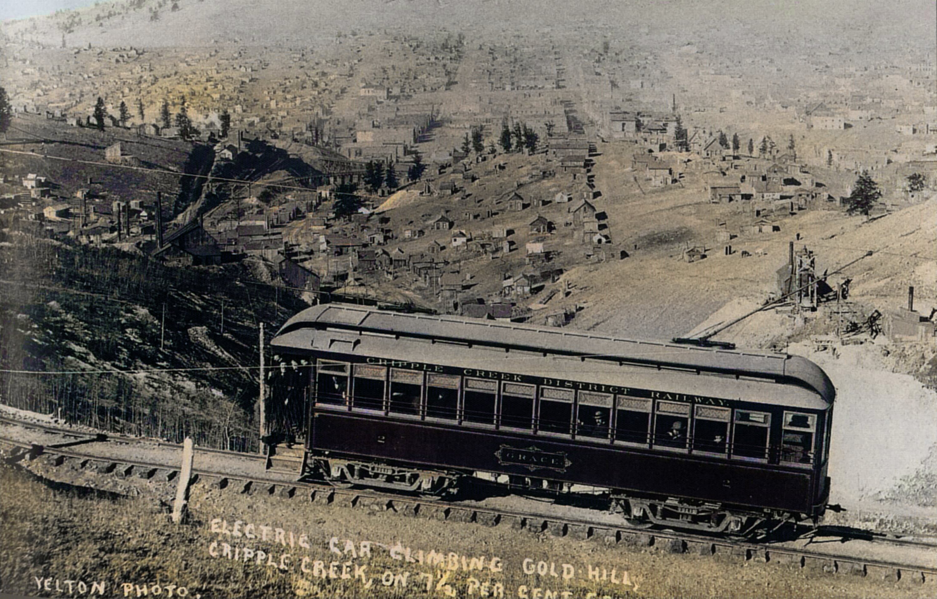 View of the Trolley car named Grace who poses on the 7.5 percent grade on the west slope of Gold Hill, climbing Gold Hill above Poverty Gulch and high above Cripple Creek, along the original steep High Line grade. In 1902 the line was rerouted over a less steep alignment.
* The two Head-frame type of mine operations seen just above the lower end/back end of the Trolley is as far as I can tell operations on the May Queen lode claim on the left and the Granite Hill lode claim on the right.
* About 2/3 up from bottom and about 1/4 in from left-hand side is the structures of the Abe Lincoln Mine, and way down in the gulch one see the M.T. Wye Trestles at the Depot grounds and to the left of them is the spur to the top of the Midland Sampler seen cutting up the hill from a spur a little down from the Abe Lincoln.
   I did procure the colored version of this image. Source was grayish, or in common speech black & white. Used an online service and tweaked and worked with image to get what looks best to my eyes at the moment.