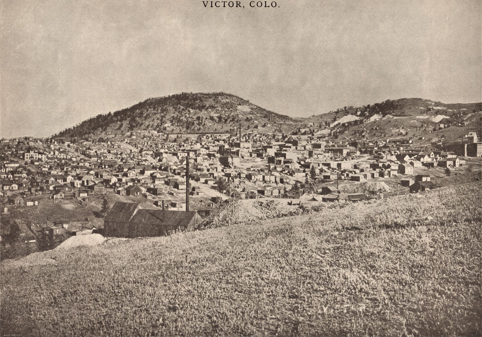 This overview of Victor as seen from somewhere in South-East  has been credited to several photographs, Schedin & Lehman is written on an Image seen at DPL, where also Julia Skolas has her name, but as this view is from after the 1899 fire which took out much of Victor, but before the head-frame of the Gold Coin was covered sometime in 1900/1901 timeframe, I can't see how she can have actually have taken this photo, so I think she bought it and the rights to it – and possible others – from the Schedin & Lehman company after she arrived at the District.
The usefulness of this image is really on the DPL view, as most of the mines are deep into the image and some of them are really not much to actually see anything other than knowing they are in this view in order to help place them in a mental map of the District/area.
* In the foreground left is the mine I've seen a close-up off from the other side, where it then was marked as "Great Central Mining & Milling Co.", and from other sources I have it linked as being named/known as the Maggie Mine.
* About middle bottom/top along the right-hand side is the top part of the Shaft-house of the Strong Mine, with the Victor High-School in front of it.
* About 2/5 down from top and about center left/right is the large smokestack of the Gold Coin mine, with the Head-frame at right of the smokestack – best seen on the DPL large image. This helps date the image except I don't know the date the head-frame was enclosed in the brick structure most common known as the Gold Coin mine.
* Above the smokestack of the Gold Coin, high up on Squaw Mtn. is a dump area seen, there is a small Shaft-house there, again I refer to the DPL as best view, that is the Nellie V. mine.
* About 1/4 in from right-hand side, and about 1/3 down from top, is the large Ajax Mine complex seen, with the big dump out over the hillside of Battle Mountain. Looking at the DPL view one can actually see they are extending the Ore-house towards right in this view.
* Just right of the Ajax is the upper shaft of the Dead Pine, located along the Golden Circle, they did as the Portland Mine did, they have a tunnel over the tracks of the Golden Circle narrow gauge line, except here it is made of wood, not steel as on the Portland property. Can't say it is on the view, I know it is there, seen as a dark spot between Ajax and Dead Pine, but it is too far away to be of any use at all.
* Further to the right, just left of the massive Portland dumps, where the hill curves, there lays the Granite Mine, seen with its Shaft-house and power house, smokestack and all, albeit at a to large distance to be of any good use for a model work, it helps in determining where in the area it was located.
* The Dillon Mine has actually two shafts seen in this view, again it is the DPL view that is really of any use to such image research, a slight distance left of the shaft-house of the Strong mine on the right-hand side, there is a small Head-frame and small hoist house seen on the hillside with a dump – that is located on the Dillon claim. Further up the hill, more hidden away due to distance and such, is the more commonly associated boxy type of Shaft-house of the Dillon seen where it lays just below the mainline of the M.T. climbing the hills towards the Portland mine area outside the view at right. Seen best on the DPL view at a 100% look, or try the 200% and go near right-hand corner, the only shaft-house in this area with lettering on the side of the structure.
* Again, the DPL is of help to locate the Ore-house of the Mary Cashen Mine, as it is poking up among the roofs of Victor structures, about halfway between the Strong and the Gold Coin mines.
* Also, on the DPL Image the Fortuna Mine is seen quite well in the 100% view, just where the word 'Skolas' is written about 2/5 up from bottom and about 1/3 in from right-hand side. Showing a small Head-Frame west of the Hoist & Power House, with what might have been the loo west of the head-frame or possible a shed for dynamite?