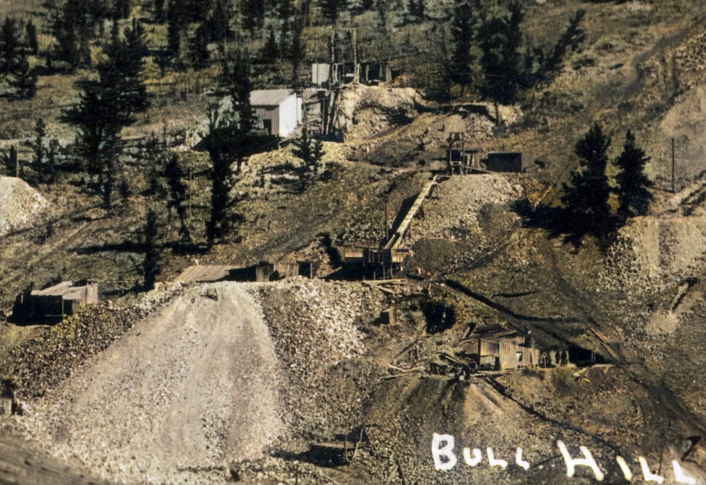This is a cropped view from a 1200 dpi scan of a postcard done by Lehr, most likely William Henry Lehr, of early Bull Hill Mines. The backside of the card is marked with a square AZO mark, indicating the card to be from the 1926 to the 1940's, but the image itself is earlier than that timeframe!
   I do not know when the photo was taken, but it can't be the timeframe the card is from as the full image has no trace of the spur up to the Blue Bird (which was built in 1903). But the High Line is there so this is from early 1898 till about early 1903, depending on when the Blue Bird spur was created. Another clue to dating this is that the mines of the Gold Sovereign and other mines has not became big operations yet.
   In fact, for this cropped view, I am guessing but I think about center of the view the tunnel that was known as the Gold Sovereign is seen, with a second tunnel, possible another claim, to the lower right. Above the tunnel, to the right, is a shaft which I think was connected to the tunnel as the claim Plat Map shows a shaft in that area. Higher up the hill in this cropped view is another shaft, which I think is the Jackson Shaft. None of those look like the huge operations seen on a 1908 image often used as postcard if of this area, just from a different angle.
   I did procure the colored version of this image. Source was grey-toned, or in common speech black & white. Used an online service and tweaked and worked with image to get what looks best to my eyes for the moment.