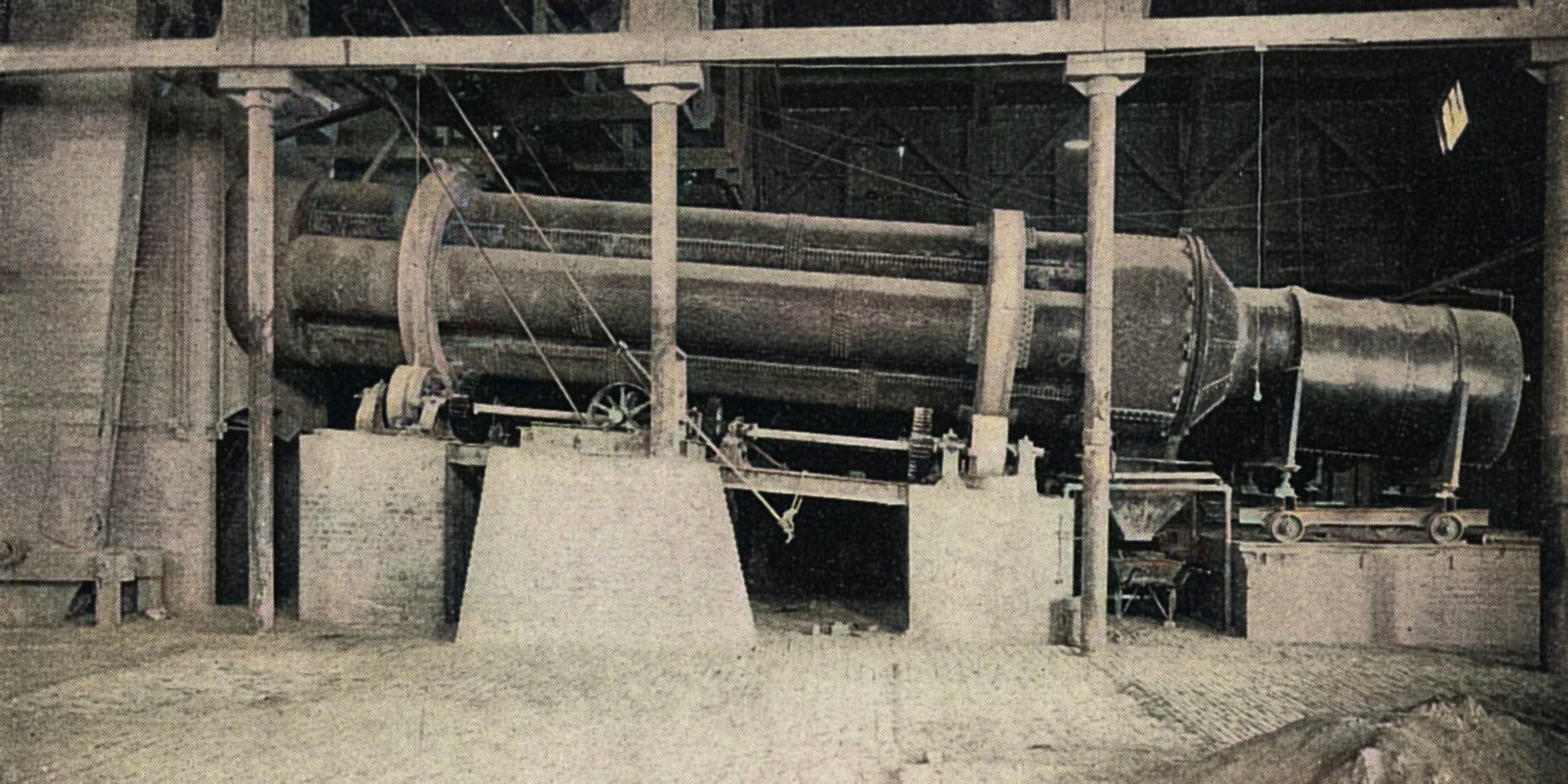 View of one of the six tubular roasting furnaces that was in use at the Metallic Mill back in 1897/98 when this image was taken. The tubular roasting furnaces was of the same general design as the dryers; 'which was four steel tubes nested together inside two track-bands and connected at the feed and discharge ends by two hoods. The tubes were lined with fireclay tile and revolve as one cylinder,' they were, however, built much stronger. The discharge was also different.
   As the text this image came with said; ''In the standard roaster the tubes are 29 ft. long by 25 in. diameter inside the lining. They make one revolution in 4.8 minutes and average 48 tons per day from 2% to 0.1% sulphur. The roasted ore is discharged continuously through a series of openings in the periphery of the hood. All these except the two over the ore-hopper at any one time are covered with a band of iron which prevents the exit of flame around the top of the furnace. The fire-box is built of steel plate and mounted on wheels. The furnace is driven with friction wheels at each track band, operated through a differential drive which insures an absolutely even motion. These furnaces are patented in the United States and abroad.''
   This seems to have been an invention by Philip Argall and hence it is named 'Argall Roasting Furnace'. I did procure the colored version of this image. Source was gray-toned, or in common speech black & white. Used an online service and tweaked and worked with image to get what looks best to my eyes for the moment.