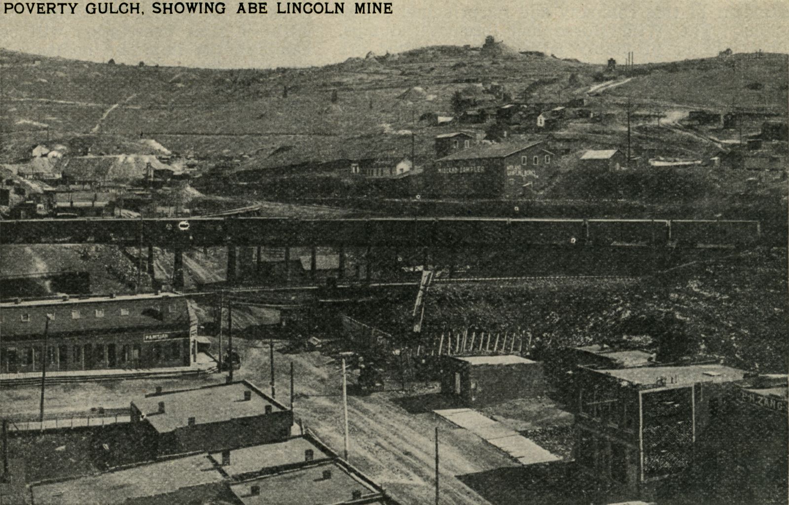   This image I've also found on the Internet at the Wyoming State Archives Photo Collection, dated as 1903 and photo by J.E. Stimson, which was a photographer of Cheyenne, Wyoming it seems. Sadly, that image is a thumbnail type only but to my eyes they are identical.
  The view itself is of a printed bad quality type showing an overlook over roof tops along Myers Avenue heading into Poverty Gulch below the trestles of the Midland Terminal Wye crossing it, with a freight train either leaving or coming into town, no engine can be seen.
  Can't identify any signs on neither copies of the image that I know about, but I do see the Midland Sampler about 1/3 down from top and about 2/5 in from right-hand side.
  The image Title mentioned Abe Lincoln mine is seen almost at left-hand edge and about 1/3 down from top, with a large dump heading out towards the right of the structures.
  On top of Gold Hill, straight up from the Midland Sampler, is seen the iconic Anchoria-Leland Mine, so easy to pick it out along the skyline.