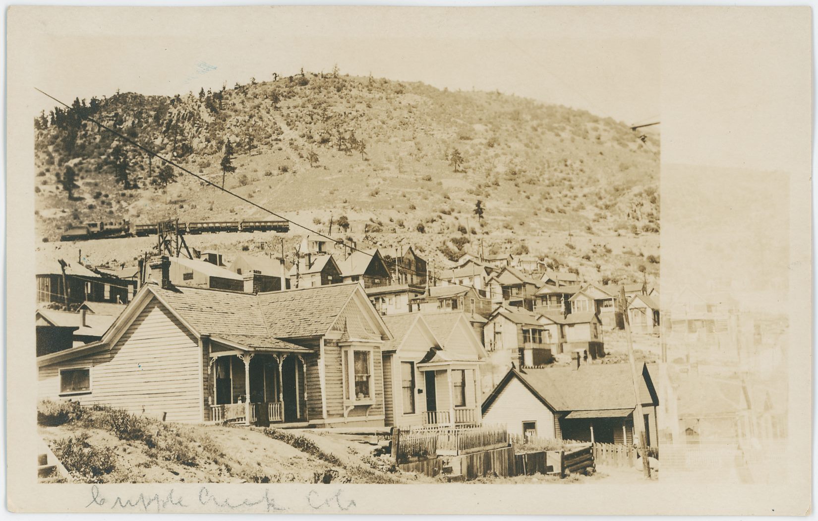 This must be along 7th Street in Victor, as there is a hanger for a trolley wire clipped off by the damaged part of this postcard. Sadly, it got damaged either in the photographing or in the making process, but still quite nice to have... Not the sharpest view but still a link back to days long gone.
   In background left, up on Squaw Mountain a short Midland Terminal train is out with 3 ore gondola type of cars, and just in front of that train there is a smaller Head-Frame poking up, which I believe is part of the Golconda Mine, as that is the only mine I know about in that area.