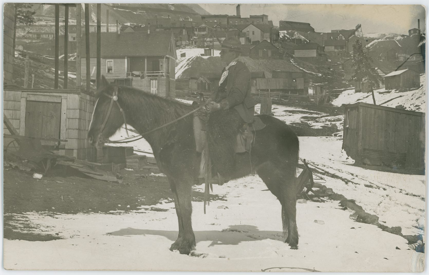 I think this image is at the eastern end of Spicer Avenue, and that the mine seen with its Head-Frame behind the head of the rider in the foreground is the Fortuna Mine, but I might be off as this been hard to decode fully where it was photographed, might be even further south in Victor.
   In background top right, about 1/10 down from top and about 1/6 in from right-hand side there is seen a trestle type poking into the image, with an Ore-House further to the left, and this is belonging to the Independence Mine, and about same down from top but 1/3 in from right-hand side is the brick structure of the Victor High School seen blocking most of the view to the Shaft House of the Independence Mine.
   Even harder to see is the Strong Mine seen mention on the backside of this card where someone has really not known their town view very well as this is clearly not on neither Victor Avenue nor 7th Street… The Strong Mine upper part of the Shaft House with a small cupola or awning poking out of the roof can be seen behind the wood posts seen near upper left. About 1/6 in from left-hand side and about 1/7 down from the top that part can be plucked out due to the awning/cupola and the window+door+window part making sort of a face on the side facing the photographer – this makes it distinct and easy to pick out.
   Along the top left-half there is seen the massive dumps of the Portland Mines and part of the Crib-wall below the No. 2 Shaft is seen, so yes, the mines really set their feel on town.