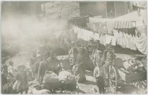 A View at Many Children Around Backyard of Houses with Sacks (Potatoes?) and Wagons, Laundry is Hanging on Lines.