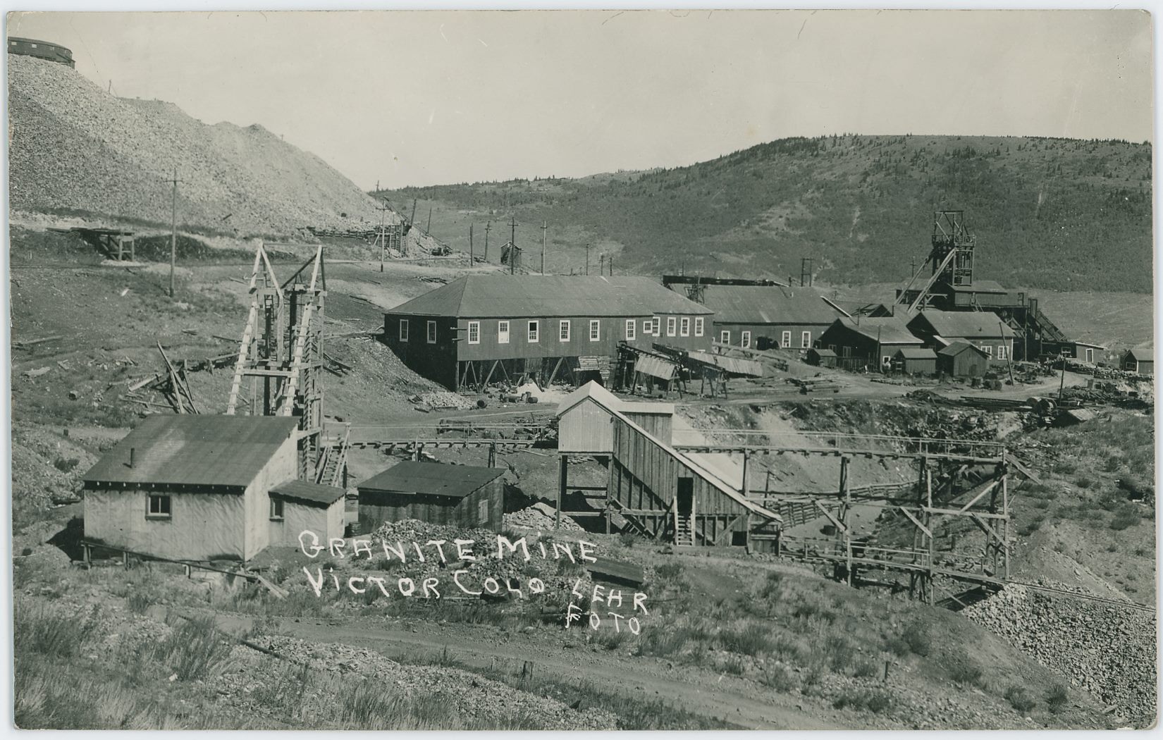 Scene shows the smaller more 'modern' Granite Mine as it was looking at the time of the photo, with the dumps of the Portland No. 2 in upper left and the Lumber Work House of the Portland No. 1 seen about 1/3 down from top and center sideways, while the Head-Frame is seen near right-hand side. The old grade of the Golden Circle ran in the 'cut' seen in lower right quadrangle – having come out from the Steel Tunnel below the Portland No. 1 dumps, part of the crib-walls is still seen in this view.
   There appears to still be track on the Short Line Ajax branch as well, seen below the Portland No. 2 dumps in upper left, track is seen about 1/3 down from top, from left-hand edge to about 2/5 into the view towards right, where it curves out of out view.