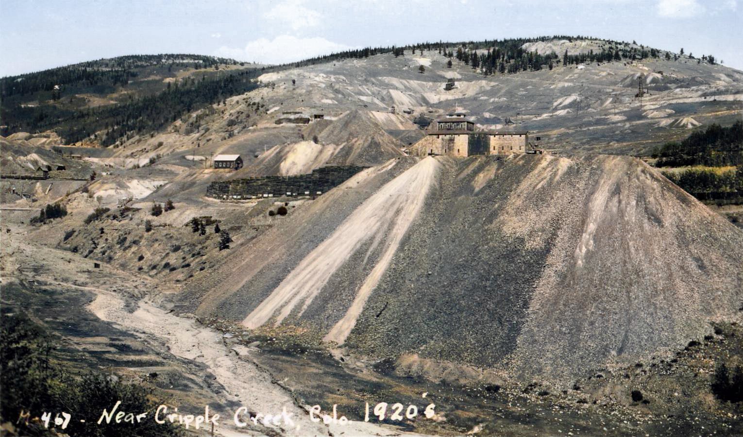 A view in Squaw Gulch towards the huge dump of the Mary McKinney Mine who's structure is popping up behind the dump, against the backdrop of Raven Hill with still a couple of mine ruins standing here and there. Image is marked to be from the 1920's, and in lower left it is still visible some flat parts, like terraces, from structures in the former town of Anaconda.
   I did procure the colored version of this image, if that is what you see, as I think it is nicer. Source is gray-toned, or in common speech black & white. Used an online service and tweaked and worked with image to get what looks best to my eyes for the moment.